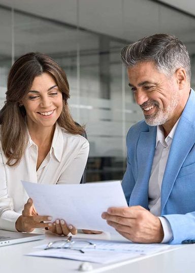 Two professionals, a man and a woman, smile while reviewing documents together.