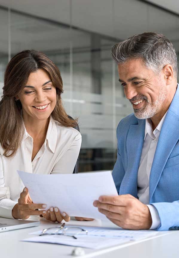 Two professionals discussing documents in an office setting, smiling and engaged.