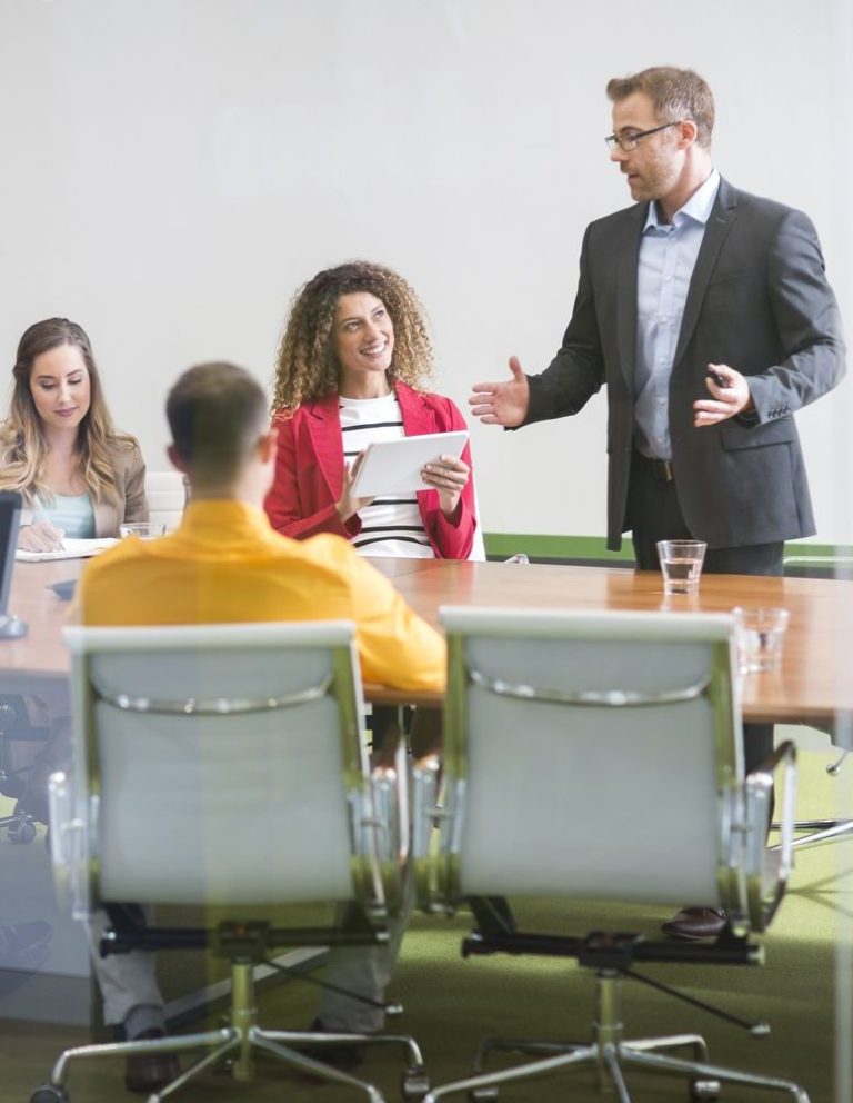 A business meeting with a man presenting to three seated colleagues.